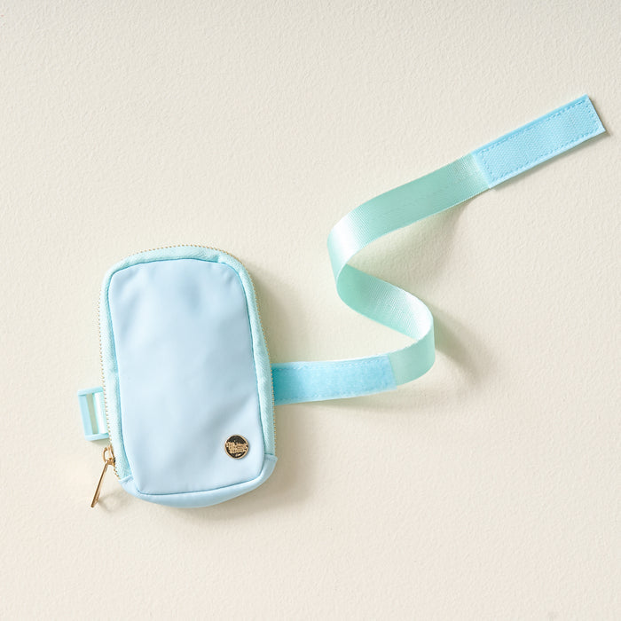 The Darling Effect's Aqua Tumbler Fanny Packโa small, stylish light blue pouch with a gold zipper and emblem, plus a matching adjustable Velcro strapโrests on a light surface. It's perfect as a water-resistant tumbler fanny pack.