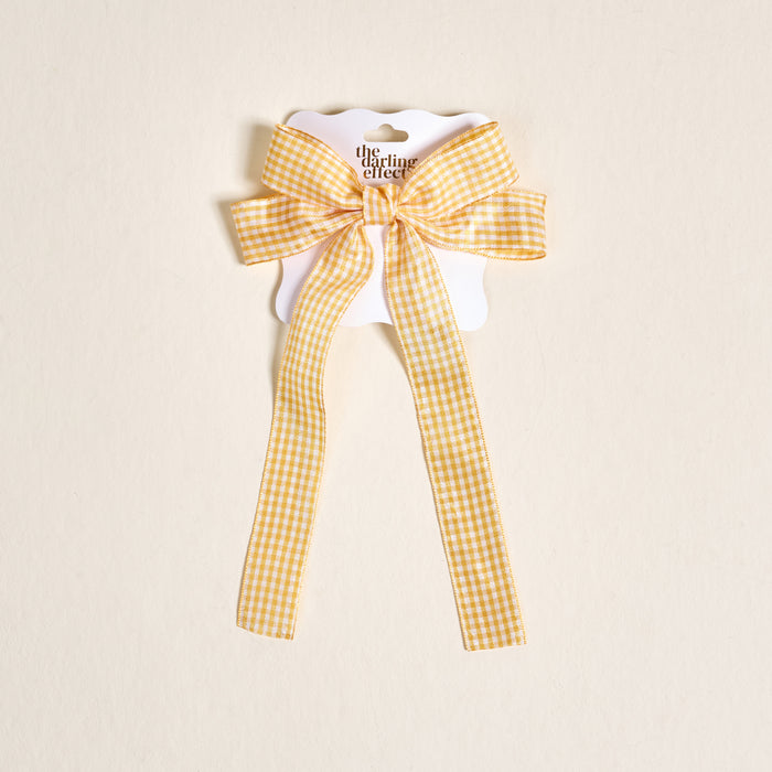 The Darling Effectβs Gingham Yellow Double Take Hair Bow, featuring yellow and white gingham long tails, is displayed on a scalloped cardβideal for lovers of charming hair accessories.