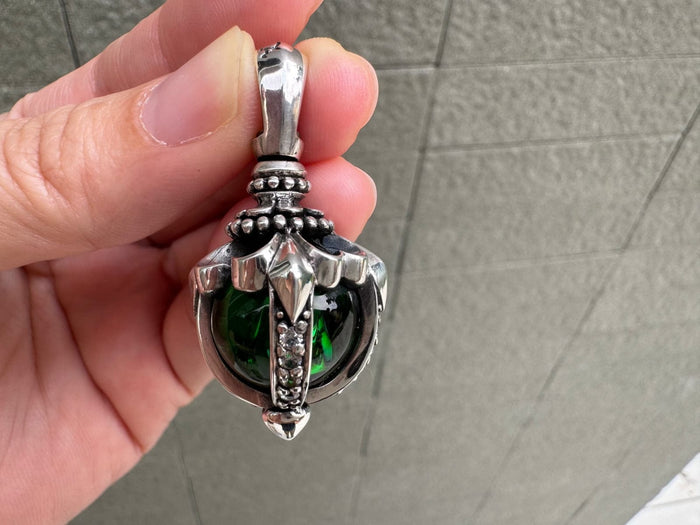 Fingers holding the pendant to reveal the pale green adularescence of the moonstone within its floral sterling silver frame.