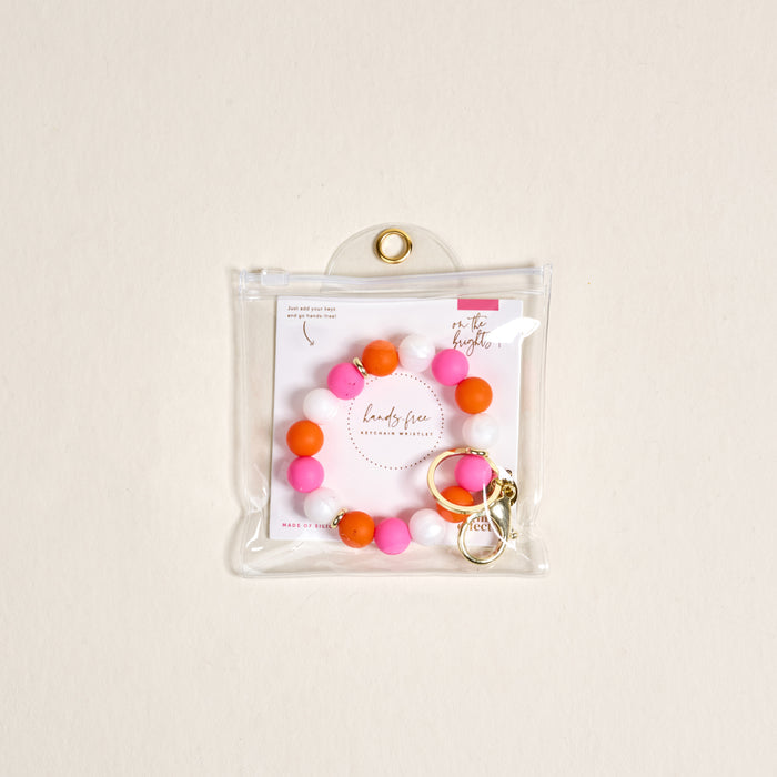 The Darling Effectโs On the Brightside Hands-Free Keychain Wristlet features pink, orange, and white silicone beads with a gold clasp, packaged in a clear zip pouch with a branded card.