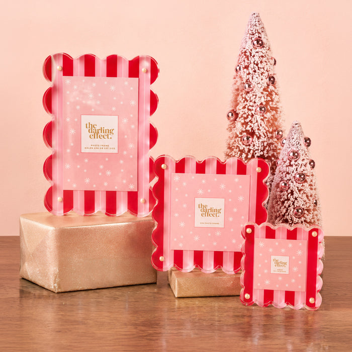 Three Peppermint Stripes Rectangle Scalloped Acrylic Frames by The Darling Effect sit on gold-wrapped boxes before glittery pink cone trees—perfect for adding modern holiday flair to your home.