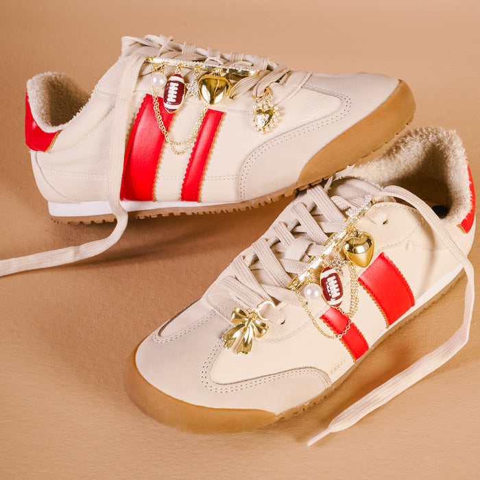 Cream sneakers with red stripes, styled with The Darling Effect’s Tailgate Time Dazzle Shoe Charm Pack featuring gold football, heart, pearl, star, and bow—unique accessories for extra flair.