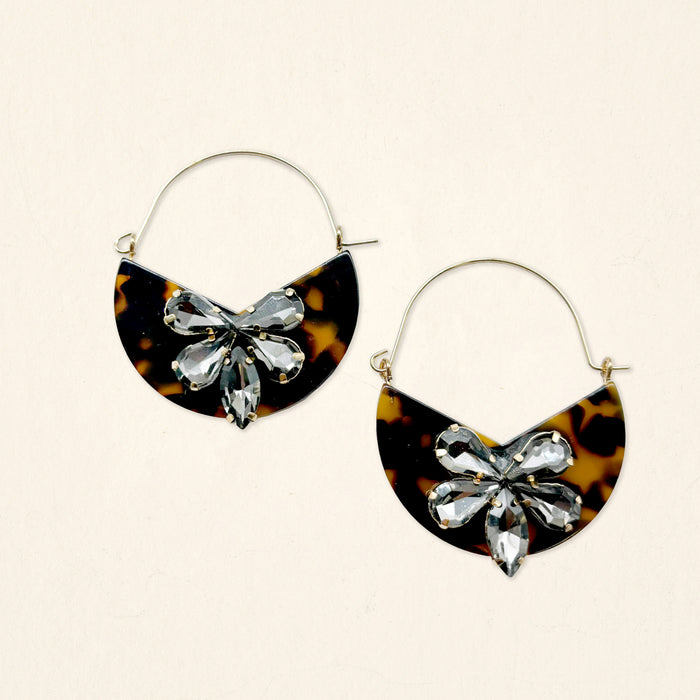 The Darling Effect's Totally Tortoise Marble Bloom Hoop Earrings feature modern hoops with half-moon tortoiseshell pendants and a central floral cluster of clear, faceted gemstones.