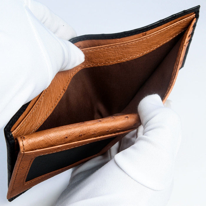 Gloved hands holding the ostrich wallet open to display its brown leather interior and quality craftsmanship.
