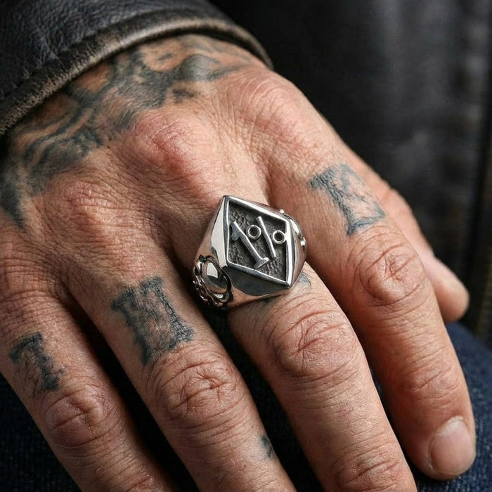 Sterling silver Outlaw 1% biker ring worn on a tattooed male hand, featuring a diamond-shaped face with a raised 1% symbol and skull side details, styled with a black leather jacket.