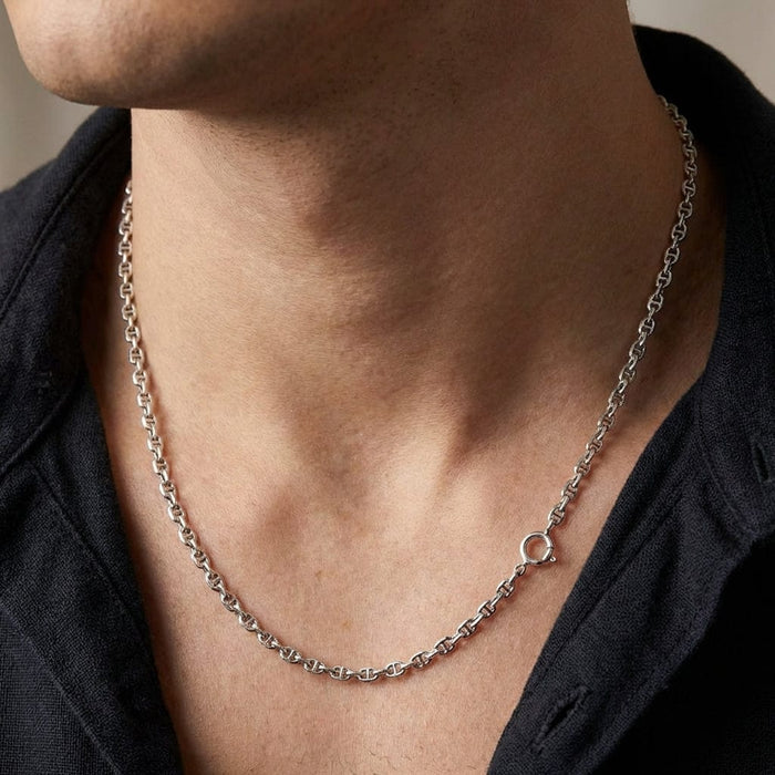 Close-up of a male model wearing a thin 2mm sterling silver anchor link necklace chain styled with a dark open-collar shirt.