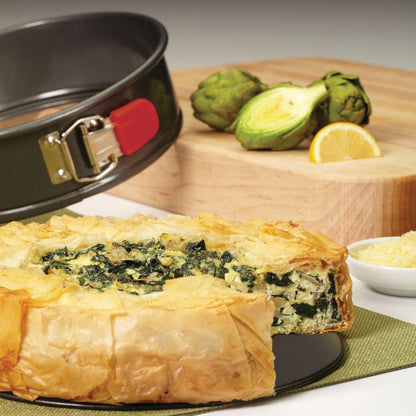 Spinach pie in a 9-Inch Nonstick Springform Pan, with artichokes and lemon on a cutting board nearby.