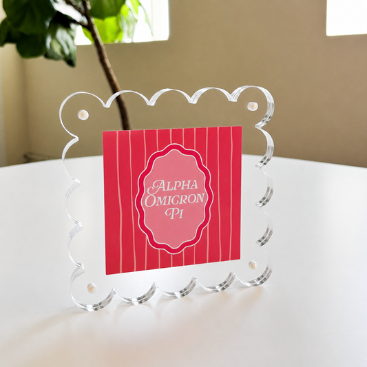 The Darling Effect’s Alpha Omicron Pi Square Scalloped Acrylic Frame features a pink card with white script, bringing a modern and decorative touch to your space.