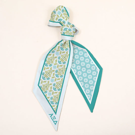 The Darling Effect’s Alpha Xi Delta Twirl & Tie Scarf Accessory showcases light blue, green, and teal floral-geometric designs with AΞΔ lettering, tied loosely for versatile styling and a sorority-inspired touch.
