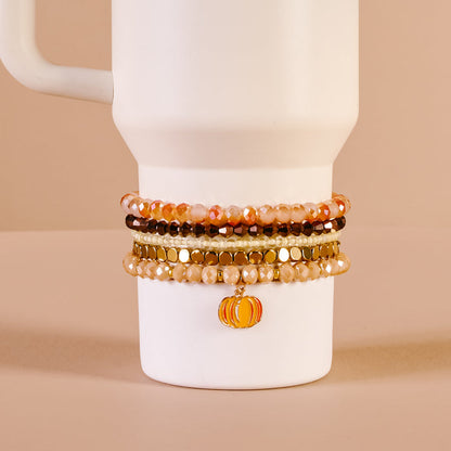 The Darling Effect's Autumn Glow Tumbler Bracelet Stack, featuring orange, gold, and brown beads with a pumpkin charm, decorates a white 40 oz tumbler cup displayed on a beige background.