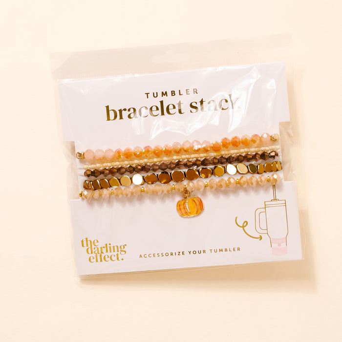 The Darling Effect's Autumn Glow Tumbler Bracelet Stack includes five fall-hued bracelets with orange, brown, gold, and champagne beads plus a pumpkin charm—perfect as stylish tumbler accessories or worn together.