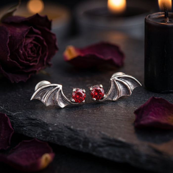 Styled on dark slate with dried burgundy roses and a black candle, both bat earrings facing inward