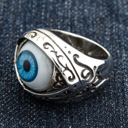 Blue iris cabochon ring photographed on denim, highlighting the wet glass dome and scrolled silver bezel
