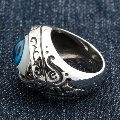 Rear three-quarter of the eye ring exposing the open inner band and shoulder scrollwork on a denim backdrop