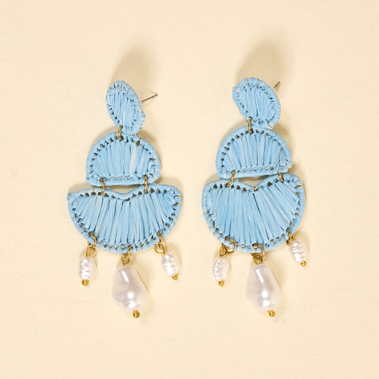 The Darling Effect’s Blue Pearl Affair Earrings are light blue, three-tiered woven boho earrings with dangling white pearls and gold accents—lightweight for everyday wear, shown on a cream background.