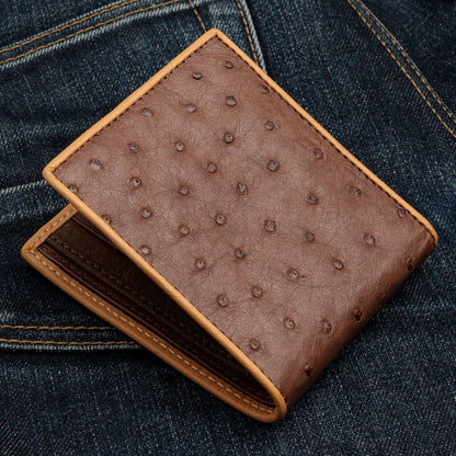 A full-quill brown ostrich wallet resting on a pair of denim jeans, highlighting its texture.