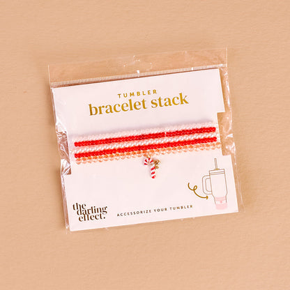 The Darling Effect's Candy Cane Crush Tumbler Bracelet Stack features red, pink, and white beaded bracelets with a candy cane charm, packaged with a tumbler illustration—ideal for tumbler accessory fans.