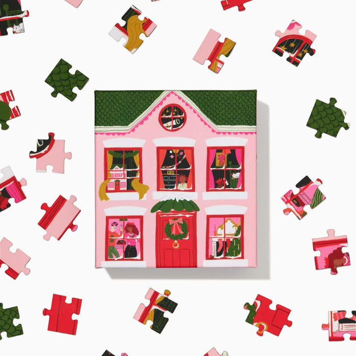The Ordinary Habit Christmas Eve 100 Piece Jigsaw Puzzle features a vibrant scene with a pink house and green roof—ideal as a colorful, festive mini puzzle for Christmas Eve.