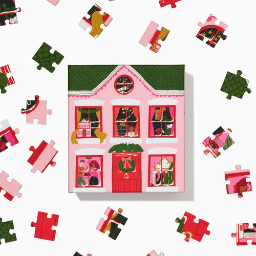 The Ordinary Habit Christmas Eve 100 Piece Jigsaw Puzzle features a vibrant scene with a pink house and green roof—ideal as a colorful, festive mini puzzle for Christmas Eve.