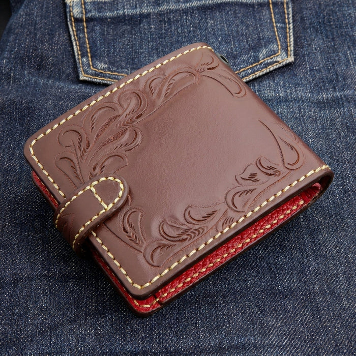 Back three-quarter view of a dark brown hand-tooled biker wallet on denim, with perimeter floral tooling and red edge.