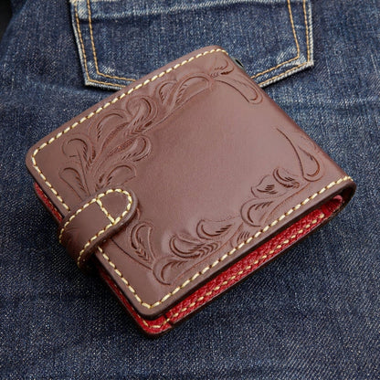Back three-quarter view of a dark brown hand-tooled biker wallet on denim, with perimeter floral tooling and red edge.