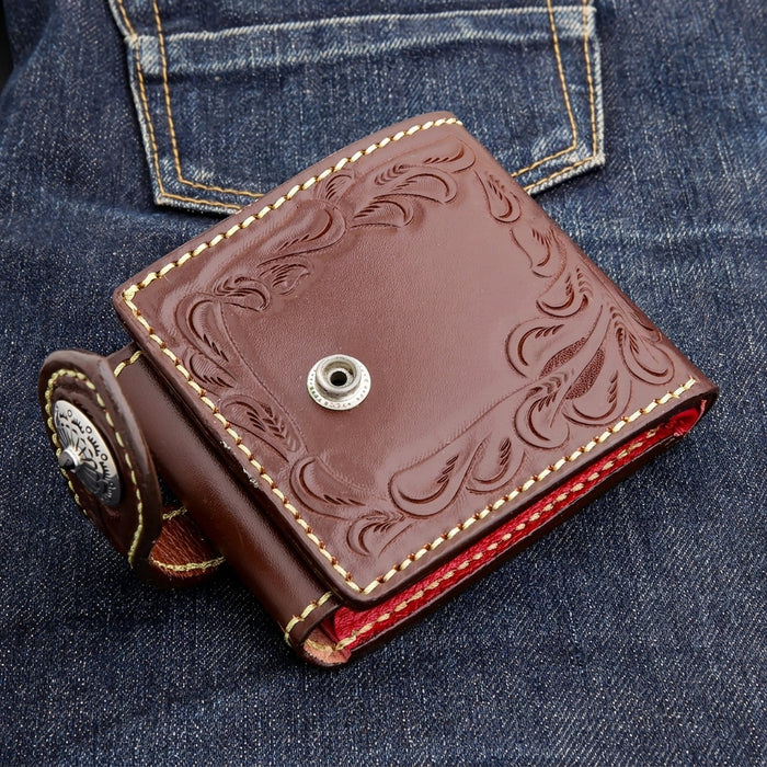 Front view of a dark brown biker wallet with the closure strap unsnapped on denim, exposing the female snap socket.