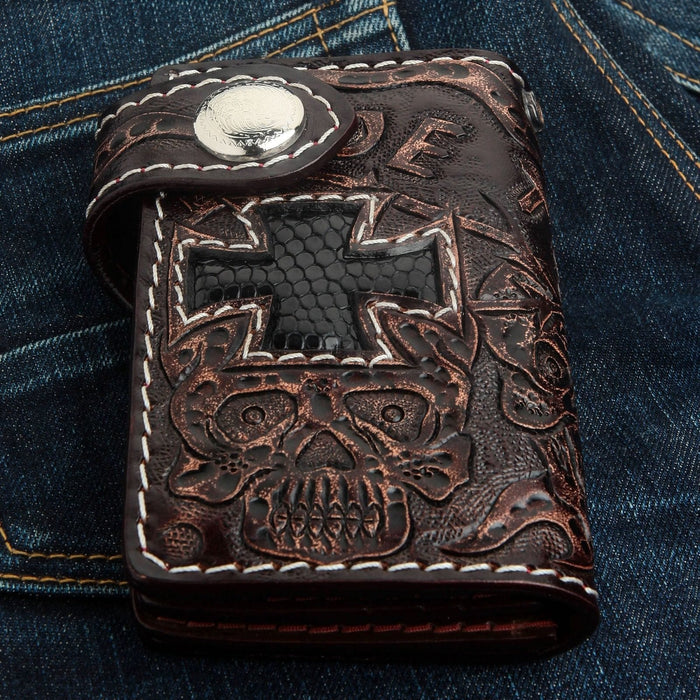 Close-up of the hand-tooled skull motif and white stitched border on the dark brown cowhide wallet.