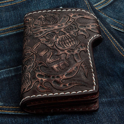 Tooled LIVE text, flames, and a skull design cover the folded dark brown cowhide wallet resting on blue denim.