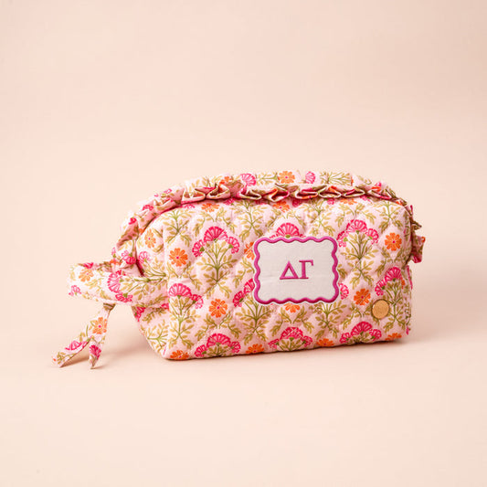 The Darling Effect’s Delta Gamma Essentials Quilted Cosmetic Pouch features pink, orange, and green floral patterns, a stitched ΔΓ patch, side knot, and gold snap—an essential sorority accessory against a light background.