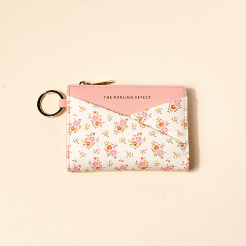 The Endless Daydream Cream Luxe Pocket Wallet by The Darling Effect is a compact vegan leather wallet with pink trim, gold zipper, keyring, and THE DARLING EFFECT logo on front. It features a pink and white envelope design with a delicate pink flower pattern.