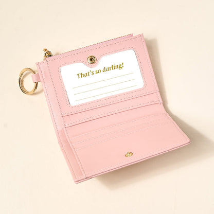 The Darling Effect Endless Daydream Cream Luxe Pocket Wallet features cream vegan leather, gold accents, a keychain, and "That's so darling!" printed inside. Its chic criss-cross design adds a stylish touch.