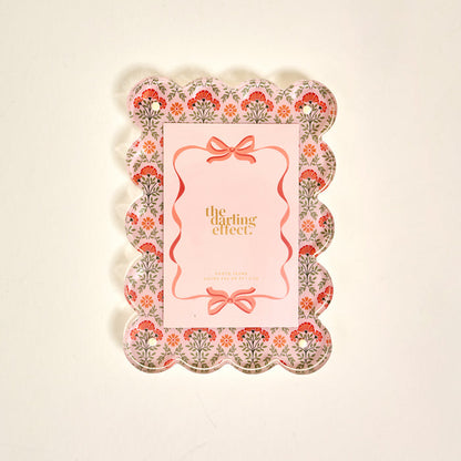 The Darling Effect’s Everbloom Dusty Rose Rectangle Scalloped Acrylic Picture Frame features pink, red, and green floral patterns and a pink center—perfect for anyone who loves stylish, modern frames.