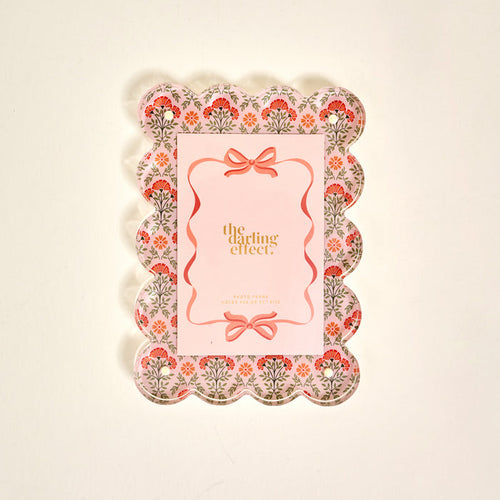The Darling Effect’s Everbloom Dusty Rose Rectangle Scalloped Acrylic Picture Frame features pink, red, and green floral patterns and a pink center—perfect for anyone who loves stylish, modern frames.