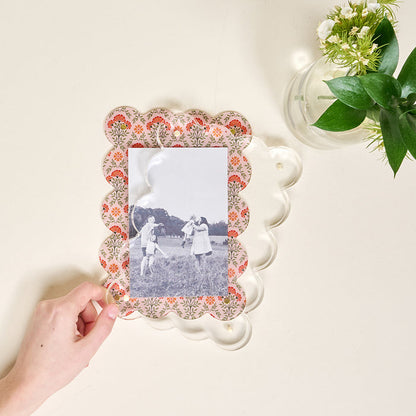 A hand places a black and white photo in The Darling Effect’s Everbloom Dusty Rose Rectangle Scalloped Acrylic Picture Frame, featuring a clear magnetized acrylic border and delicate floral accents.