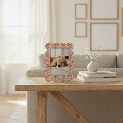 The Everbloom Dusty Rose Rectangle Scalloped Acrylic Picture Frame by The Darling Effect displays a photo of a sleeping dog on a wooden table beside stacked books and a small vase, with wall art and a sofa adding to the cozy setting.