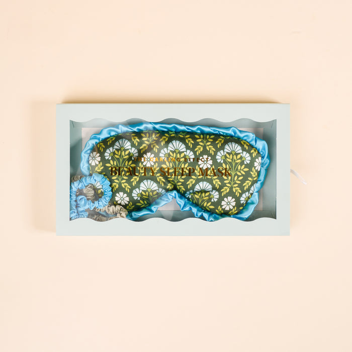 The Darling Effect Everbloom Forest Green Beauty Sleep Mask set includes a floral eye mask with blue trim and matching satin scrunchie, all in a light blue window box. The mask features a green background with white and yellow flowers.