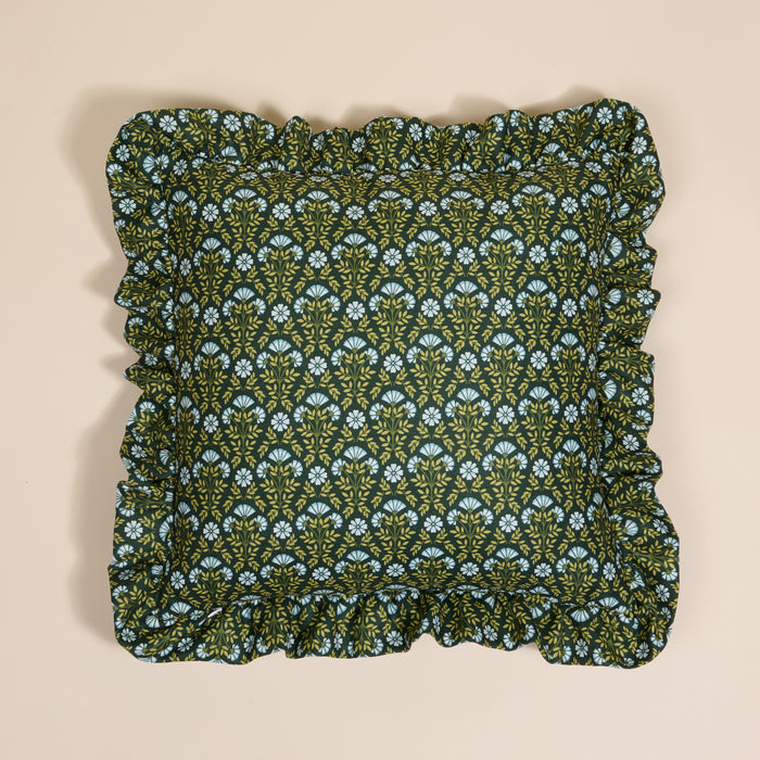 The Darling Effect’s Everbloom Forest Green Scalloped Square Throw Pillow features a floral pattern in light blue and yellow, paired with ruffled edges—a cozy accent layered on a neutral beige background.