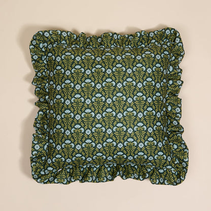 The Darling Effect’s Everbloom Forest Green Scalloped Square Throw Pillow features a floral pattern in light blue and yellow, paired with ruffled edges—a cozy accent layered on a neutral beige background.
