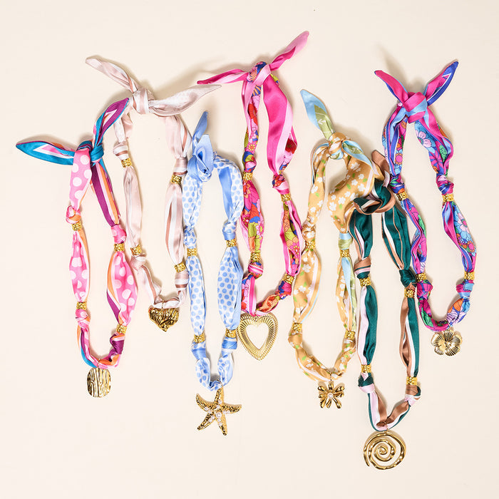 The Darling Effect’s Evergreen Twist Make a Statement Scarf Necklaces—featuring artful patterns, gold-tone beads, and metallic heart, star, shell, and spiral charms—are showcased side by side on a light background for a bold look.