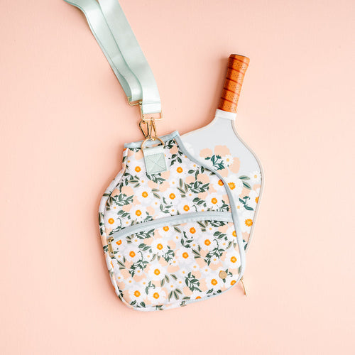 The Darling Effect's Flower Talk Pickleball Case features a light blue floral design and light green strap, shown partially covering a paddle with a brown grip—perfect for stylish pickleball players.