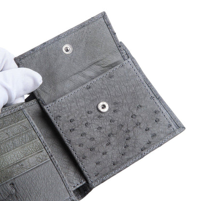 A detail shot of the grey ostrich wallet's interior, with a gloved hand opening the snap-closure coin pocket to show its construction.