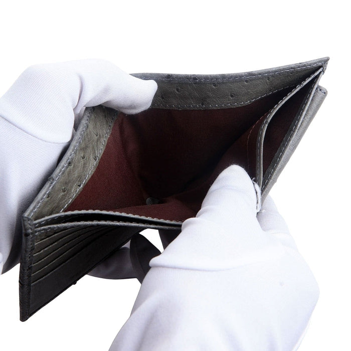 The supple grey ostrich leather wallet being held open by gloved hands to show its flexibility and the fabric-lined bill compartments.