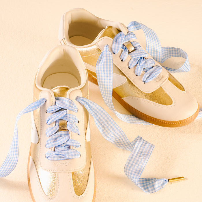 Two white and gold sneakers with Gingham Light Blue Step It Up Shoelaces by The Darling Effect, featuring durable laces that add style and flair.