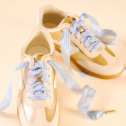 Two white and gold sneakers with Gingham Light Blue Step It Up Shoelaces by The Darling Effect, featuring durable laces that add style and flair.