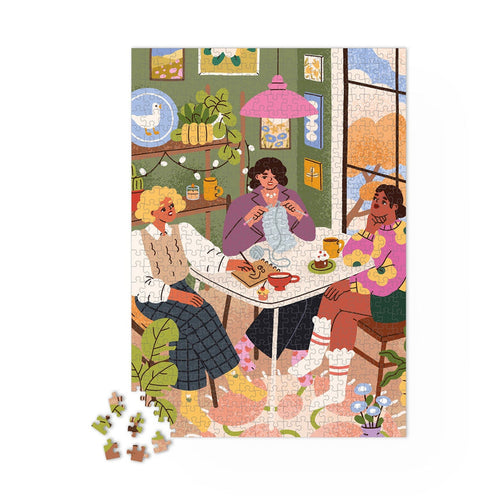 Three women chat and sip tea in a cozy room as they work on the Maison Joliette "Girlfriends" 1,000-piece jigsaw puzzle. Surrounded by knitting supplies and plants, they enjoy this beautifully crafted puzzle, made in France.