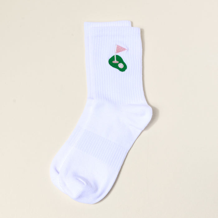 The Darling Effect Golf Embroidered Crew Socks: a white women's sock with a green putting green and pink flag design near the cuff, shown flat on a light beige background—ideal for fans of colorful, embroidered socks.