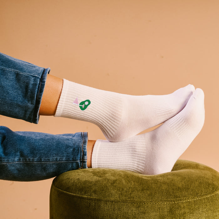 Someone wearing The Darling Effect's Golf Embroidered Crew Socks with blue jeans rests their feet on a green textured ottoman, set against a tan background.