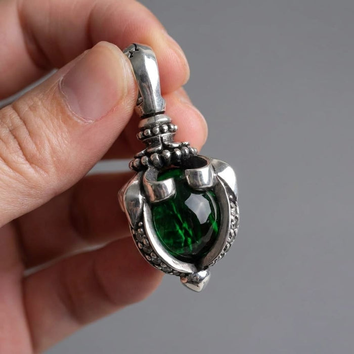 A close-up view of a hand holding a detailed sterling silver gothic pendant featuring a large, deep green moonstone set in a tribal claw design against a neutral grey background.