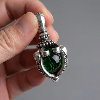 A close-up view of a hand holding a detailed sterling silver gothic pendant featuring a large, deep green moonstone set in a tribal claw design against a neutral grey background.