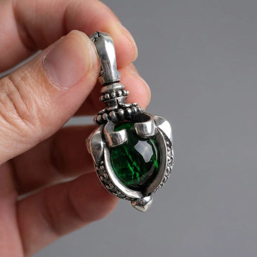 A close-up view of a hand holding a detailed sterling silver gothic pendant featuring a large, deep green moonstone set in a tribal claw design against a neutral grey background.
